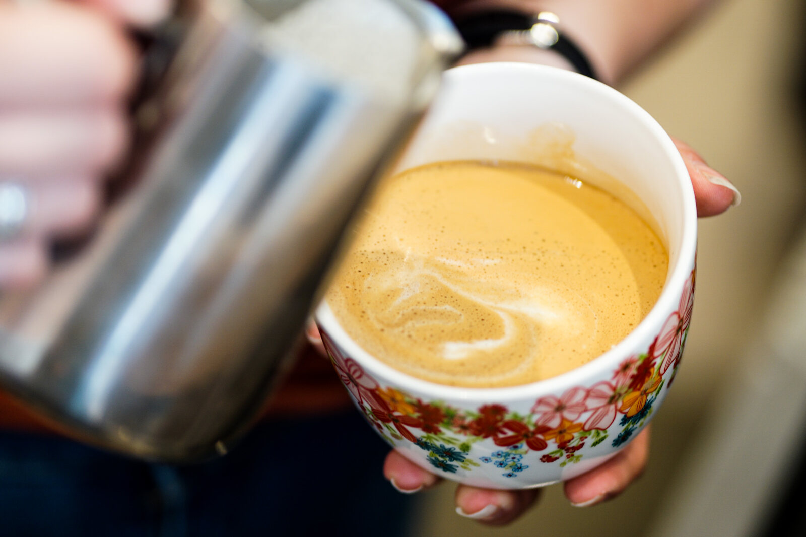 A latte being poured into a floral cup